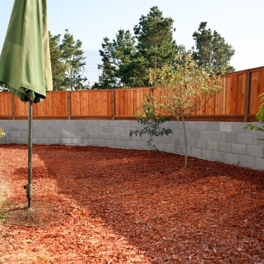 Fence on top of a retaining wall in a backyard with a green umbrella